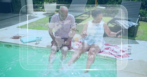 Senior couple sitting poolside dipping feet while woman using smartphone in backyard