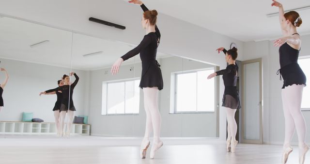 Group of ballet dancers practicing in a studio with mirrors, wearing black leotards and white tights. Useful for content related to dance classes, performing arts education, teamwork, and disciplined training routines. Mirrors and clean ambiance highlight professional practice environment, ideal for artistic and fitness blogs.
