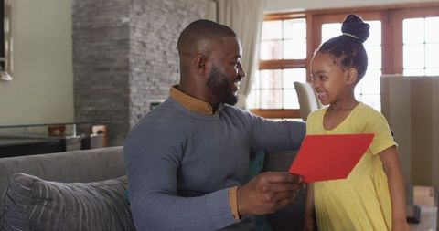 Daughter Presenting Handmade Gift to Smiling Father at Home