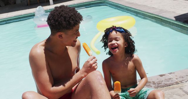 Father and son sitting by edge of outdoor swimming pool, sharing laughs while attempting to eating orange popsicles, bright floaties visible floating in pool. Perfect for illustrating family bonding, summer fun, holiday promotions, childhood joy, and outdoor leisure activities.