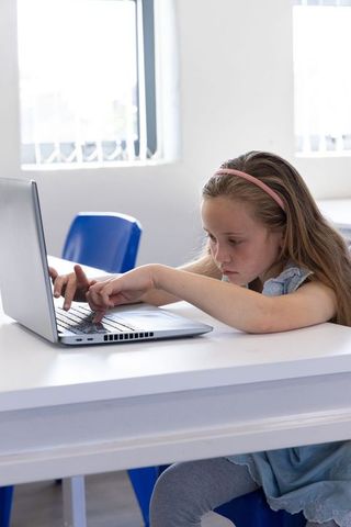 Young girl concentrating on laptop while studying in modern classroom with natural light
