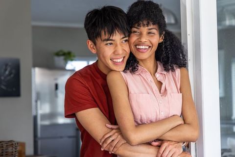 Multicultural couple embracing in doorway showing ring, smiling in kitchen home romantic moment