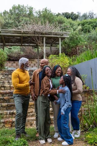 Multigenerational african american family laughing together on garden terrace near pergola
