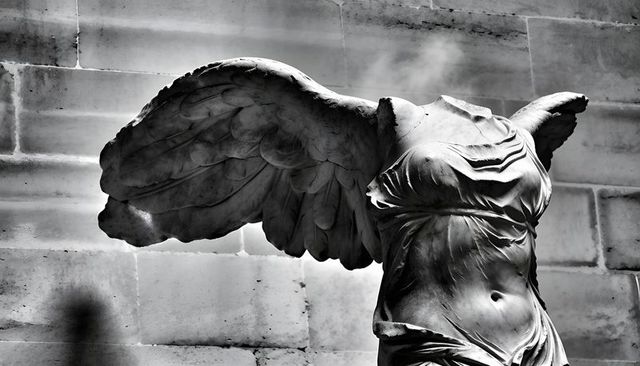 Headless winged victory torso capturing draped marble folds against weathered stone wall