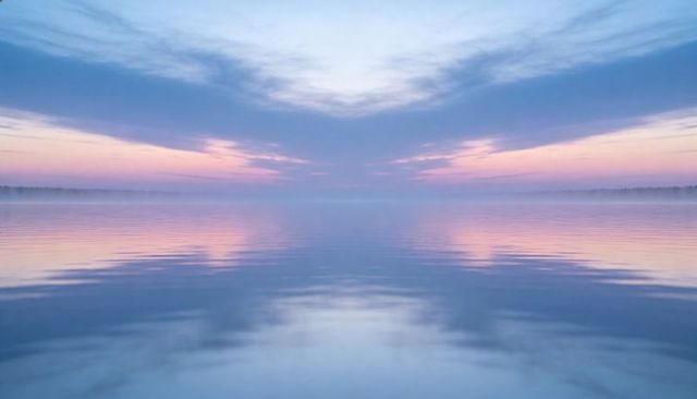 Pastel sunrise reflecting on calm glassy lake with misty treeline and serene symmetry