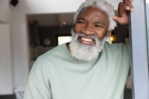 Senior african american man smiling and leaning on doorframe in sunlit modern home