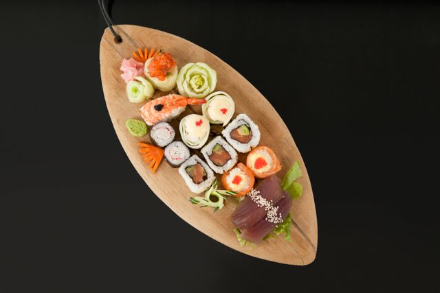 Assorted sushi set served in wooden boat plate against black background