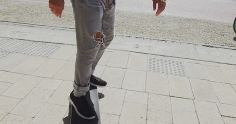 Male Skateboarder Balancing on Tiled Sidewalk in Ripped Jeans