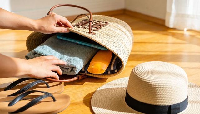 Packing straw tote with towel, sunscreen and tablet for beach getaway, travel essentials