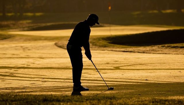 Silhouette golfer addressing ball on sunlit fairway in morning golden light