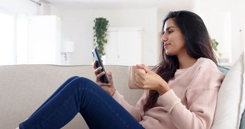 Relaxed Woman Using Smartphone and Enjoying Coffee at Home