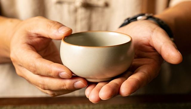 Hands holding small handcrafted ceramic tea bowl in warm intimate closeup for tea ritual