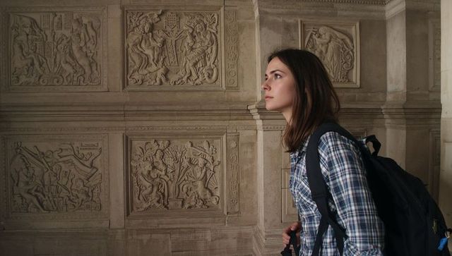 Young woman exploring historic stone reliefs in gallery with backpack and plaid shirt