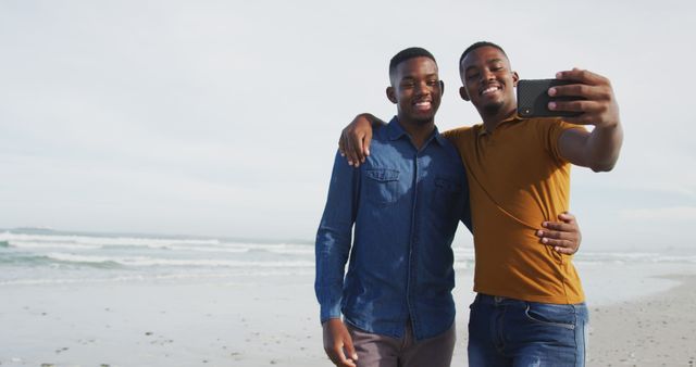 African american twin brothers standing on a beach using a smartphone. healthy outdoor family leisure time together.