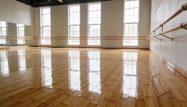 Sunlit ballet studio reflecting windows on glossy parquet floor with mirrored wall and barre