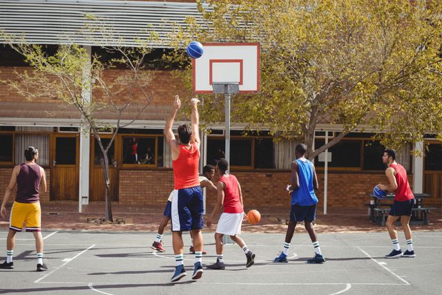 Group of basketball players practicing on an outdoor court. Ideal for use in sports-related content, fitness promotions, team-building activities, and youth recreation programs. Highlights teamwork, athleticism, and outdoor activity.