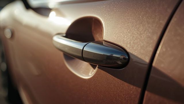 Glossy black car door handle on metallic bronze panel casting shadow and reflecting surroundings