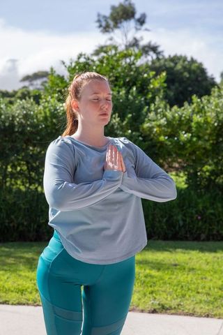 Woman practicing yoga prayer pose outdoors in park