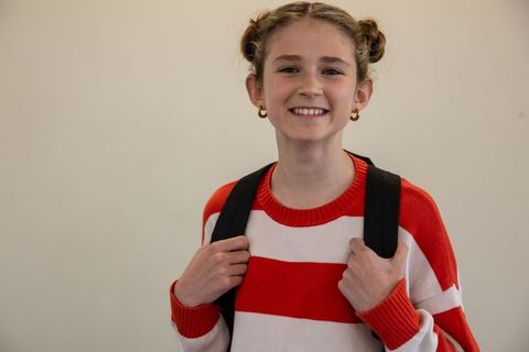 Smiling girl with backpack against off-white wall