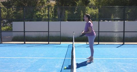 Woman playing paddle tennis on blue court holding paddle near net outdoor sunlit lifestyle