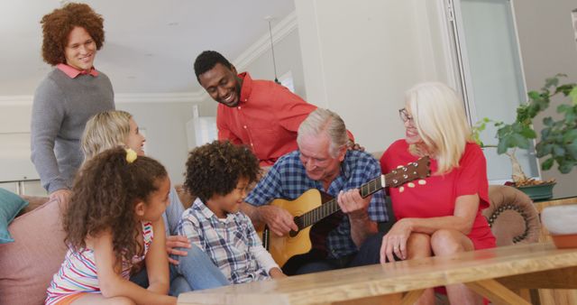 Image of diverse family siting on the couch and grandfather playing the guitar. Family life, spending time together with family.