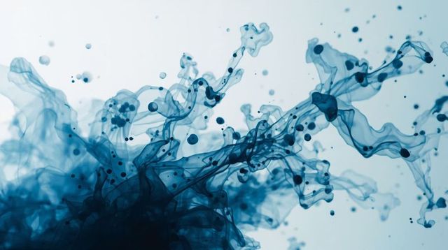 Deep blue ink swirling in water creating fluid ribbons and droplets