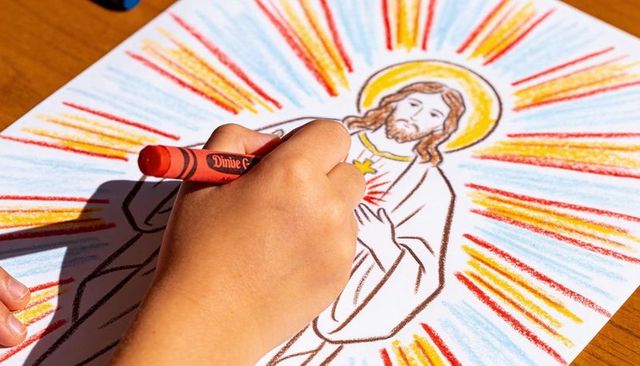 Child coloring sacred heart of jesus with red crayon in classroom religious art activity