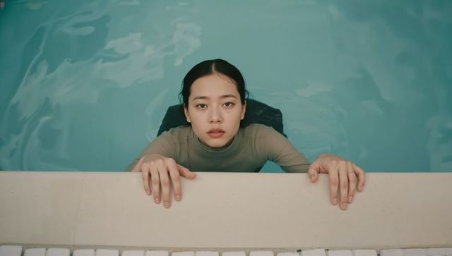 Overhead holding pool edge gazing upward asian woman wearing rash guard in turquoise pool