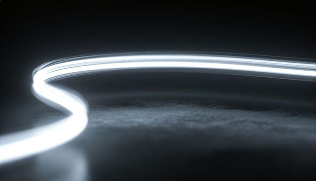 Glowing s-curve light trail creating double reflection on low-lit monochrome surface
