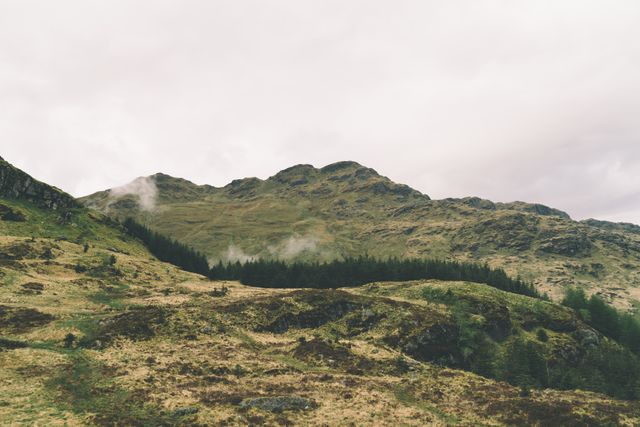 Misty highland landscape featuring forested hills under an overcast sky. Perfect for nature-related content, travel inspiration, outdoor activities, and environmental awareness campaigns. Suitable for backgrounds in websites, brochures, and promotional materials highlighting serene and untouched natural beauty.