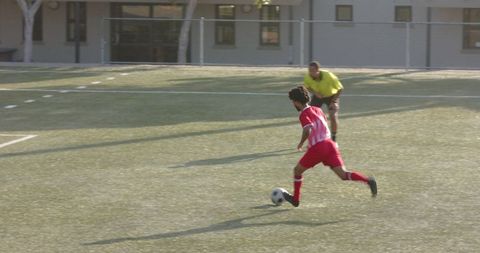 Soccer player in motion with referee observing on grass field