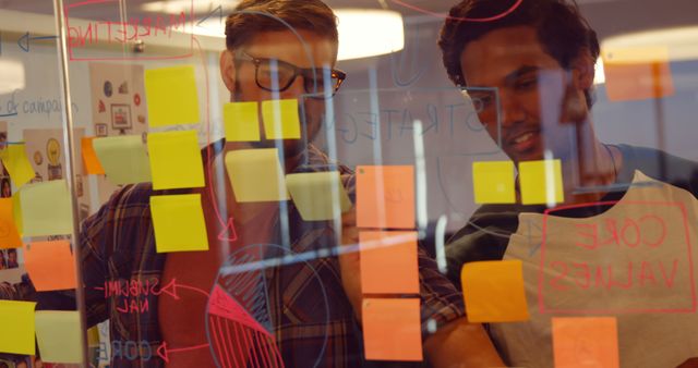 Young professionals brainstorming ideas on glass board with sticky notes - Download Free Stock Images Pikwizard.com