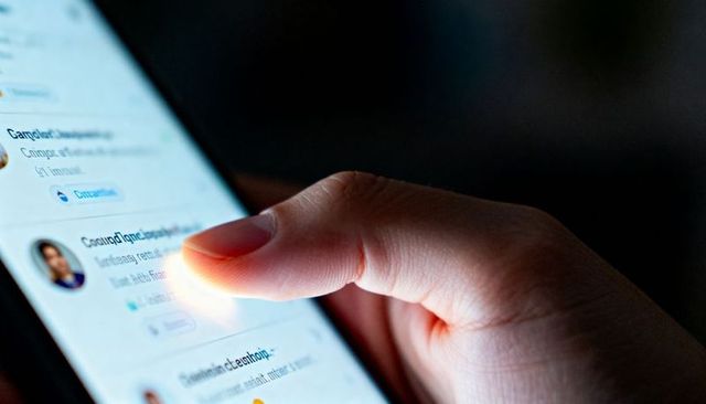 Tapping thumb pressing smartphone screen in low-light closeup with glowing message list
