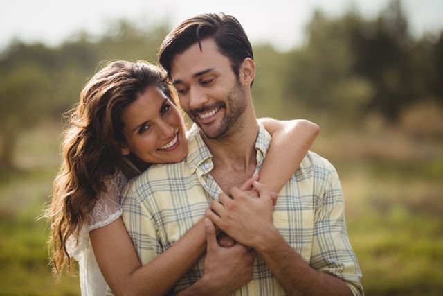 Young couple embracing and smiling outdoors on a sunny day, perfect for use in advertisements, relationship blogs, lifestyle magazines, and social media posts promoting love, happiness, and outdoor activities.