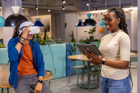 African American coworkers testing VR headset while facilitator using tablet in lounge