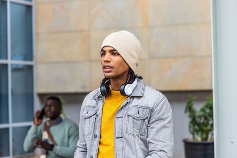 Young african american man in beanie and headphones wearing yellow sweater and denim jacket