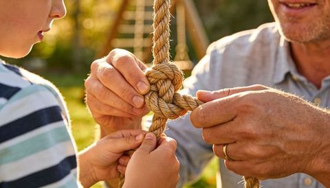 Father teaching son tying sturdy rope knot on backyard swing at golden hour
