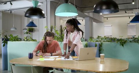 African american coworkers collaborating in modern coworking space with laptop notes and plants