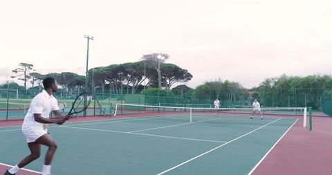 Doubles tennis match on outdoor hard court with players in white preparing at net