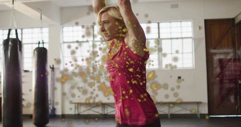 Woman raising arms during boxing training with dynamic particle effects in bright gym