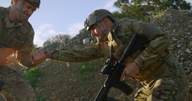 Two soldiers are training in a rugged outdoor environment. One soldier helps the other by extending his hand. They are wearing full tactical gear including helmets and camouflage uniforms, giving a sense of camaraderie and support. This image could be used for themes related to military training, teamwork, assistance, and preparedness in challenging conditions.