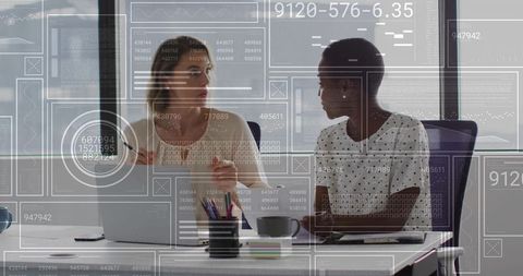Female Colleagues Collaborating on Data Visualization in Modern Office with Digital Overlays