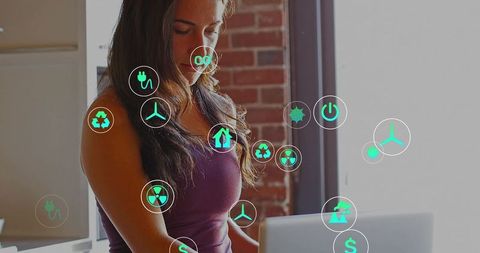 Typing woman wearing maroon tank working on laptop with renewable energy icons overlay