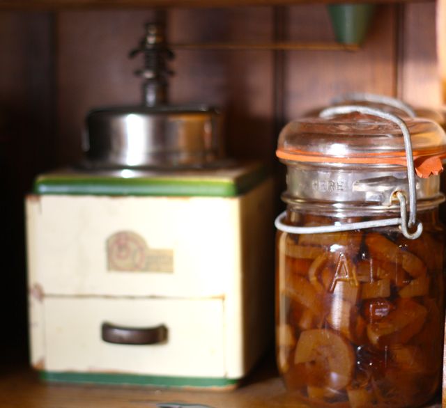 This image captures a vintage kitchen setting with an antique coffee grinder and a glass jar of preserved fruit. Ideal for use in advertisements for kitchen decor, retro-themed cafes, and articles on preserving food or vintage kitchenware. Perfect for creating nostalgic and rustic ambiance in marketing materials and blogs.
