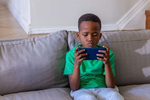 African american boy playing mobile game on sofa at home, focused child using smartphone