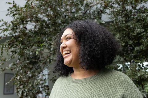 African american woman laughing in indoor atrium wearing sage green sweater among plants