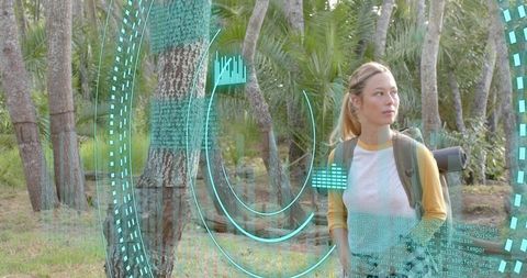 Hiker scanning holographic teal data interface while trekking through palm grove with backpack
