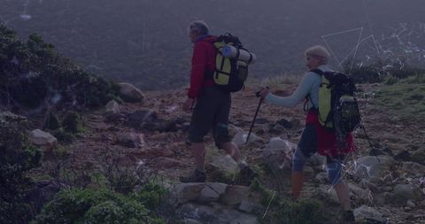 Senior couple hiking rugged mountain trail with gear