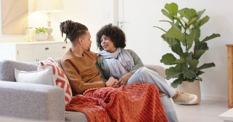 Diverse couple sharing cozy moment on sofa under rust orange throw in modern living room