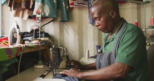 Man sewing in his workshop with a sewing machine, showcasing the craft of tailoring. Useful for content focusing on small businesses, craftsmanship, vocational skills, and tailoring services. Image can be used in articles, blogs or promotional materials about artisans and entrepreneurs.